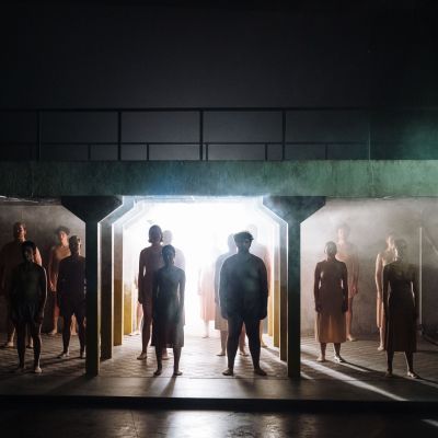 Chorus silhouetted by strong lighting standing under the top level of the set